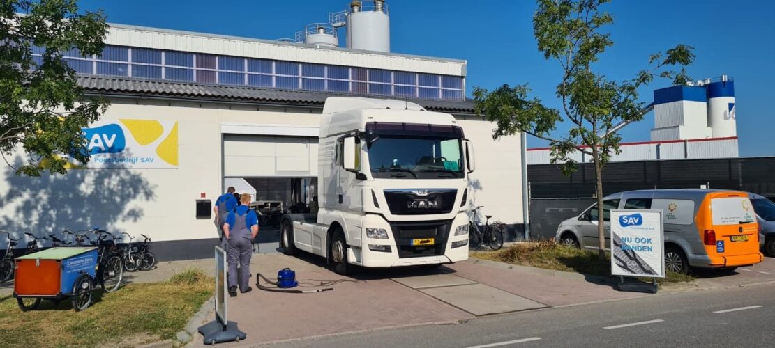 Grote vrachtwagen voor de loods. Hij past niet door de deuropening.